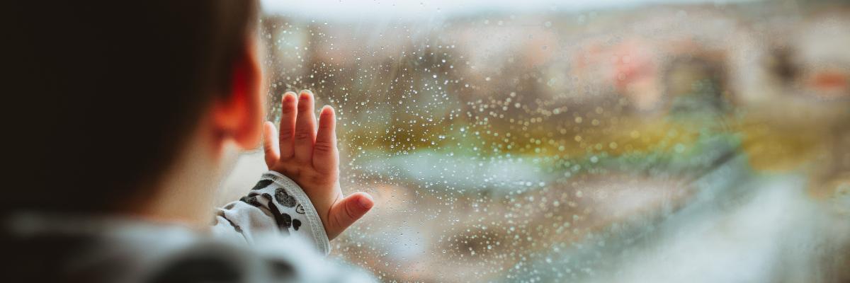 Jong kind dat zijn raam tegen het glas houdt, kijkend naar buiten