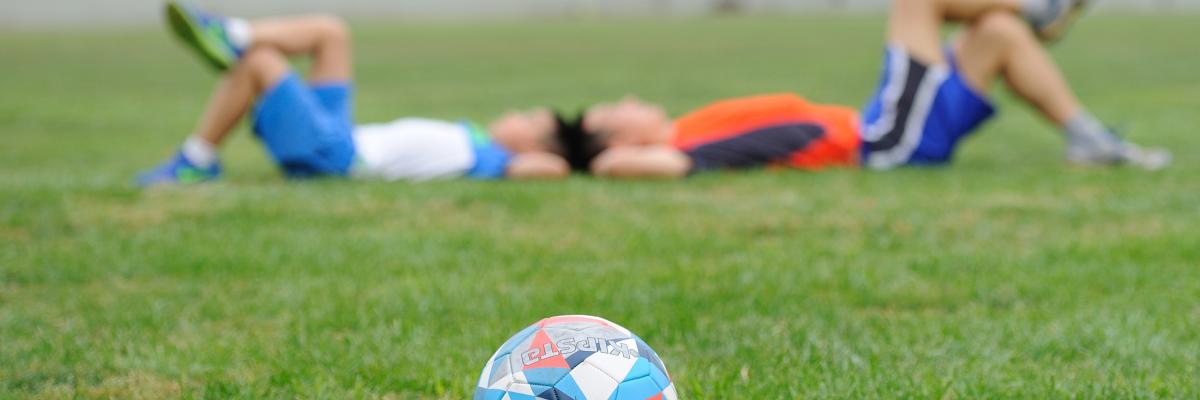 Twee jongens liggen hoofd aan hoofd in een grasveld met een voetbal op de voorgrond.