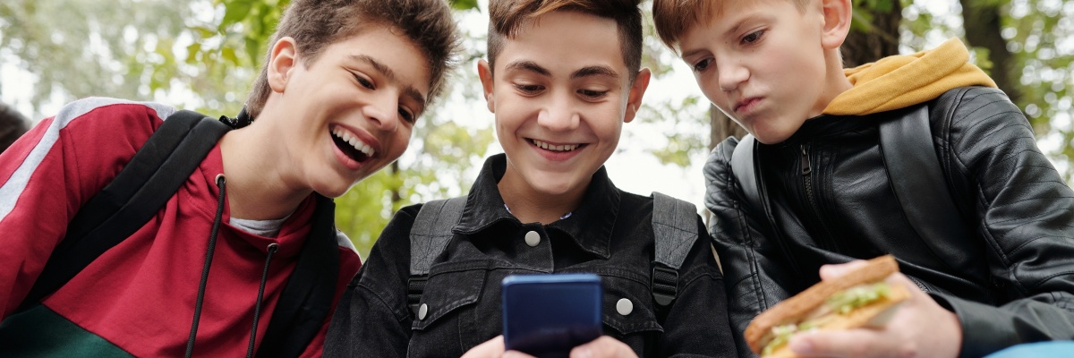 Drie tienerjonges die glimlachend kijken naar de middelste zijn telefoon.