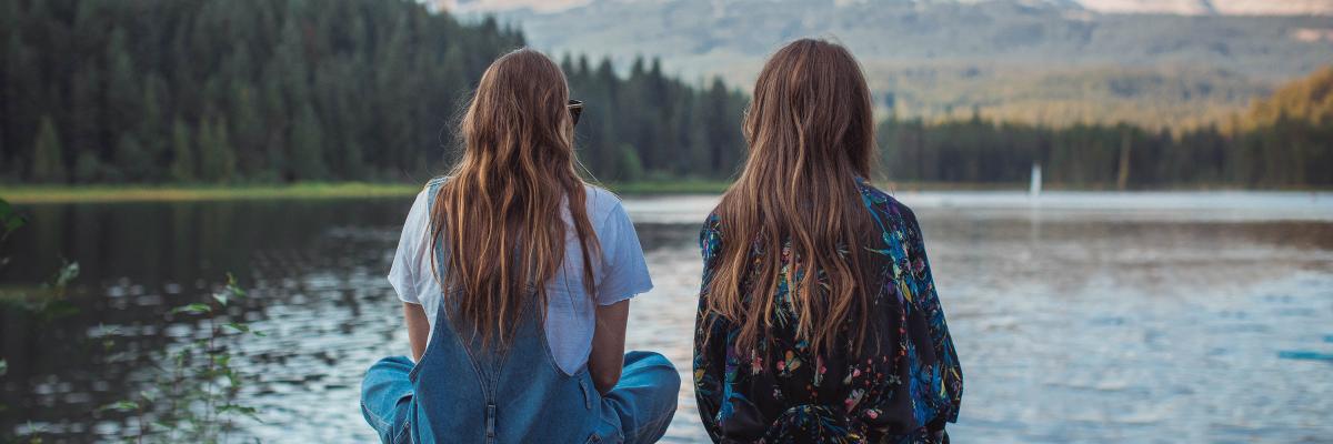 Twee jonge vrouwen, zitten te staren over het water, wij zien hun rug