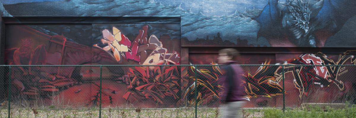 Een muur vol mooie grafitti, we zien een schim van een jongere die er voorbij wandelt.