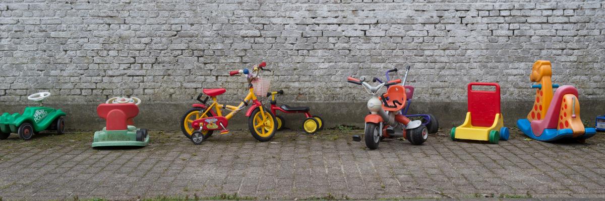 Allemaal kinderspeelgoed op een rij: een loopfietje, een voortduwertje, ...