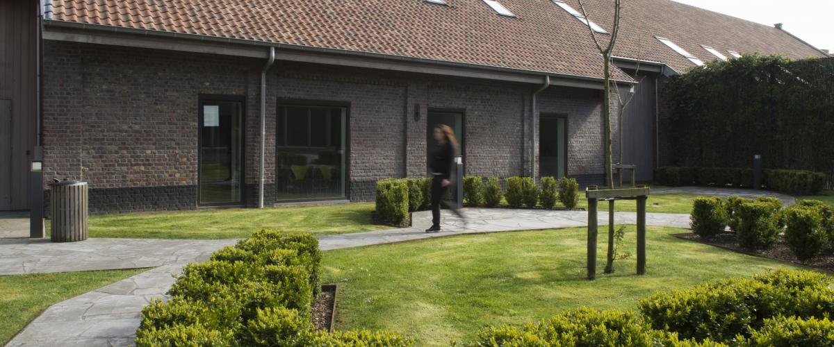 Een deel van de binnentuin. Je ziet een meisje voorbij wandelen op het pad tussen het gras.