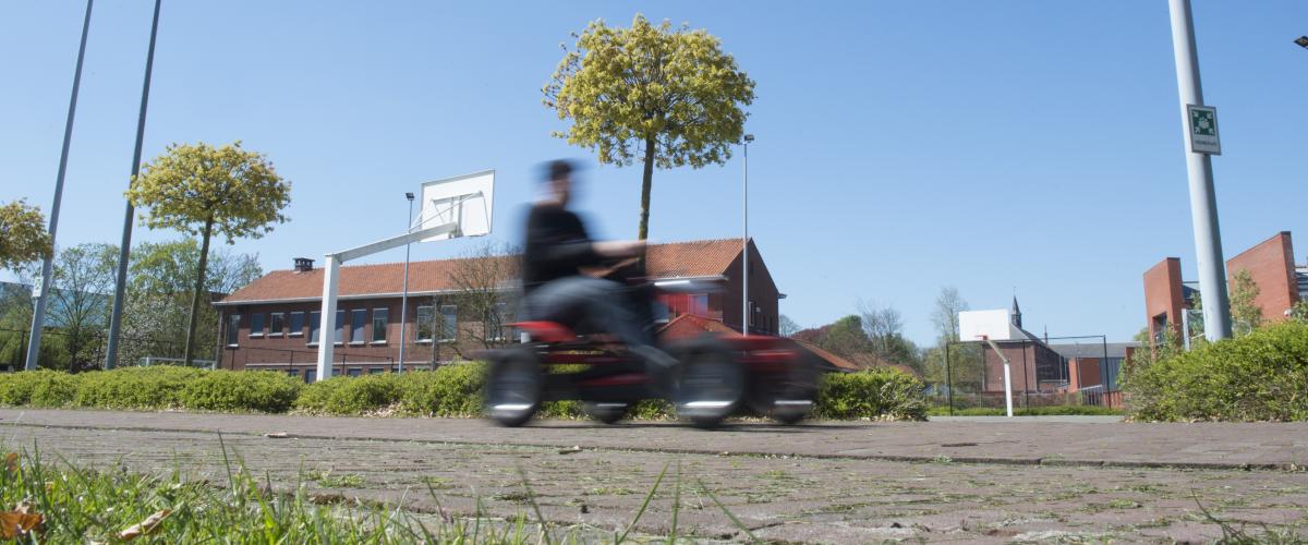 De binnenplaats waar wat bomen staan. Je ziet een jongere op een go-cart voorbij rijden.