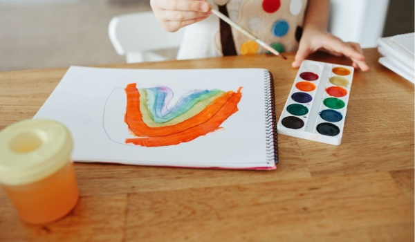 Een meisje schildert een regenboog met waterverf en een penseel