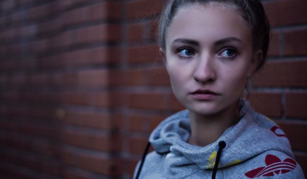 Jonge vrouw die over de schouder kijkt en voor een bakstenen muur