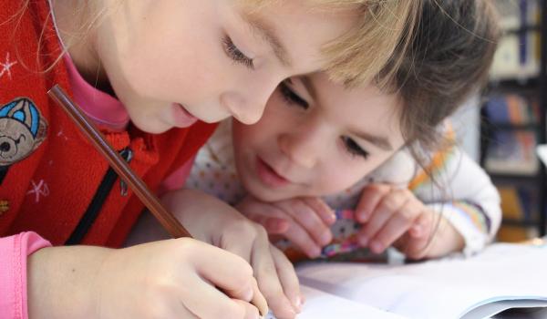 Twee meisjes waarvan één met potlood in een boek aan het schrijven is.