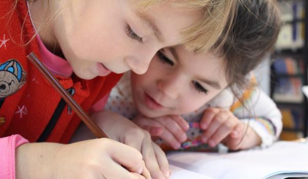 Heel jonge meisjes, die samen iets in een schriftje schrijven