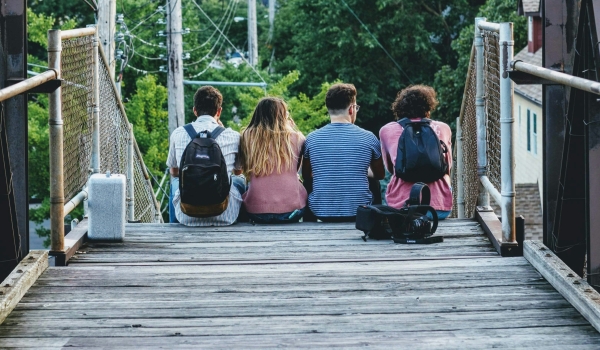 Vier jongeren zitten met hun rug naar de camera op een hangbrug