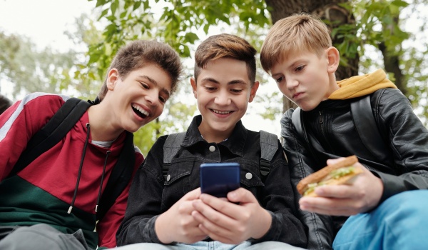 Drie tienerjonges die glimlachend kijken naar de middelste zijn telefoon.