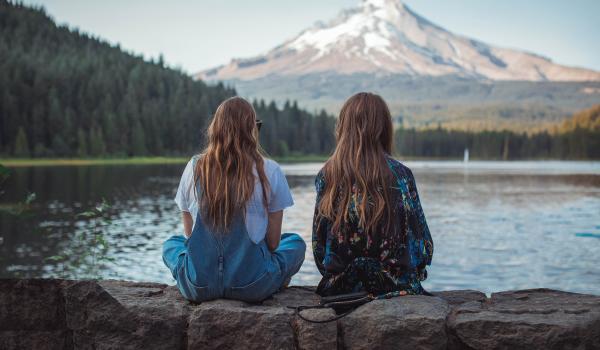 Twee jonge vrouwen, zitten te staren over het water, wij zien hun rug