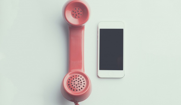 Oude rood-roze telefoonhoorn naast een nieuwe iphone.