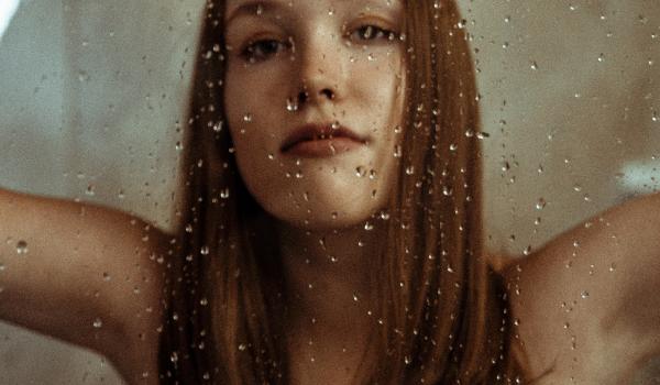 Jonge vrouw, achter glas met regen op