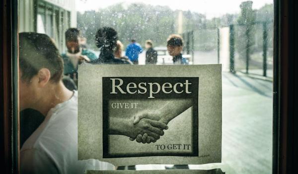 De jongeren van de gemeenschapsinstelling gaan naar binnen, op het raam plakt een affiche over respect