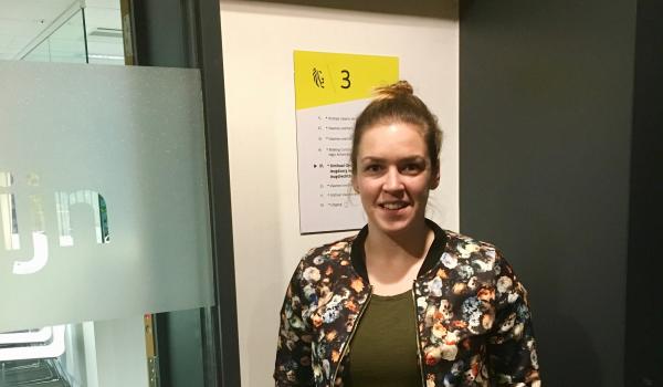 Charlotte Thomas staan met een fleurig jasje en opgestoken haar voor een raam