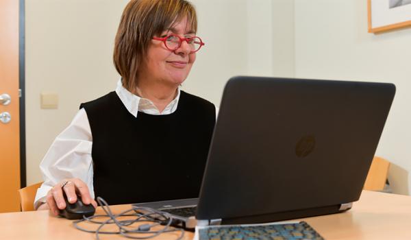 Een dame met een rode bril en halflang bruin haar, achter de laptop
