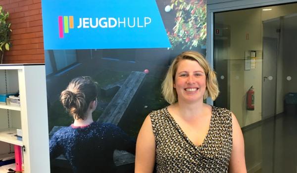 Femke Brack, staat glimlachend voor een roll-up van Jeugdhulp