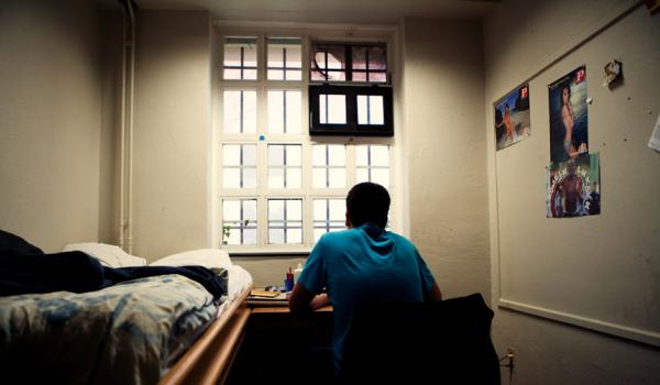 Een jongere op zijn slaapkamer, starend uit het raam. Zijn rug is naar de kijker gedraaid