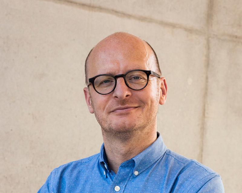 Jan Brocatus, met een zwarte bril en een blauw hemd