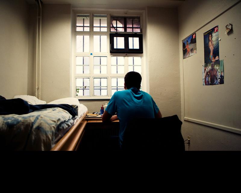 Een jongere op zijn slaapkamer, starend uit het raam. Zijn rug is naar de kijker gedraaid